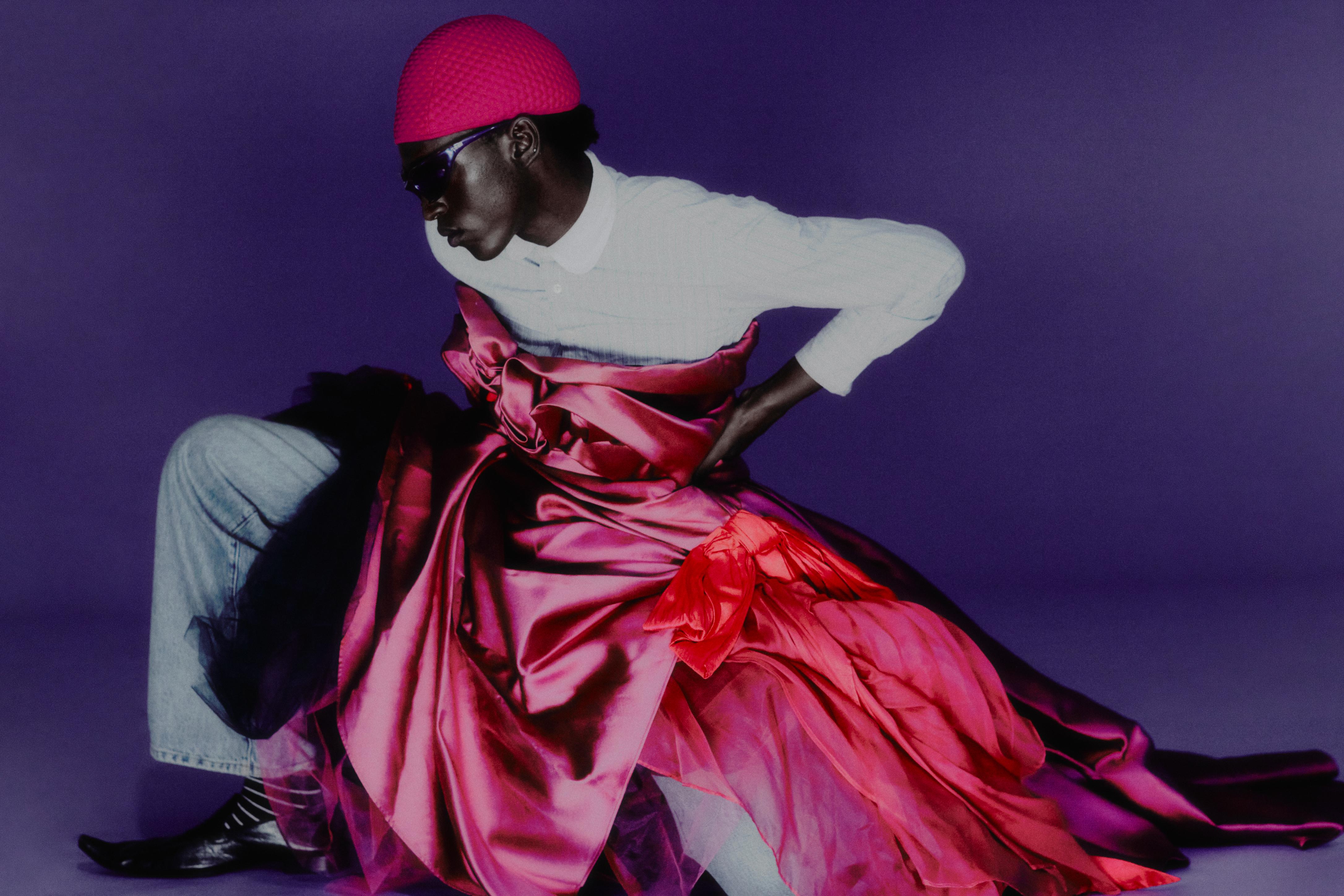 Light blue striped shirt _ Ralph Lauren; Red knit hat _ Prada; Blue high-waisted jeans _ Loewe; Purple layered dress _ Vivian Luk Atelier; Purple cat sunglasses and black leather pointed loafers _ Balenciaga