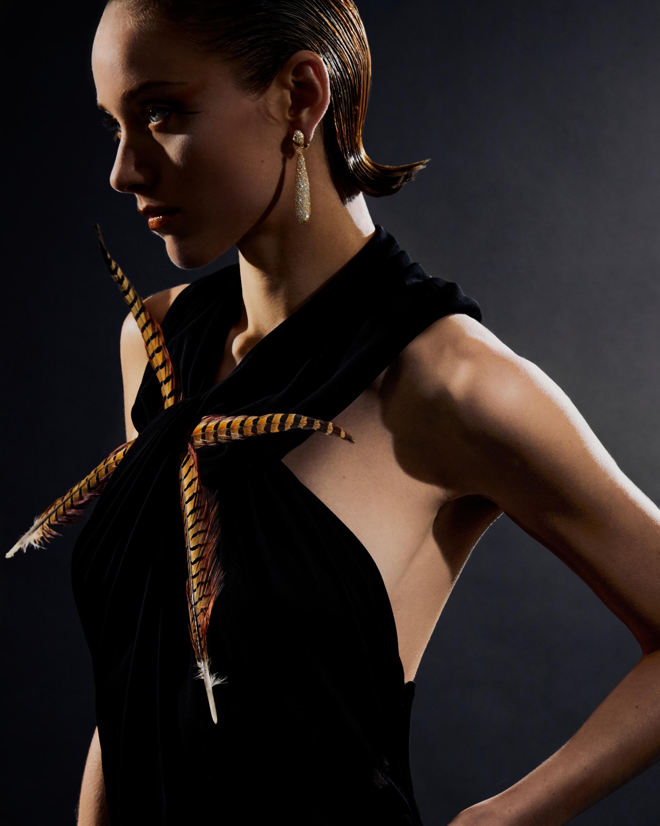 Talisman cocktail earrings in yellow gold _ De Beers; Black dress with feather detail _ Loewe